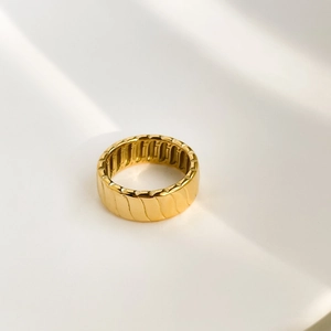 Detailed close-up of wide golden geometric ring featuring diagonal textured grooves