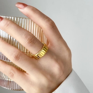 Minimalist gold ring with vertical ribbed texture shown on a hand holding a glass cup