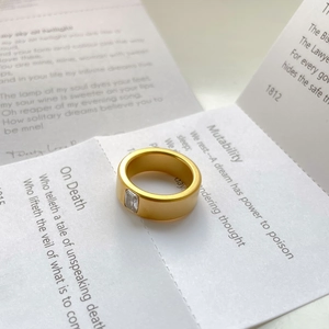 Detail of matte gold titanium ring with a square zircon set on a white poetry card