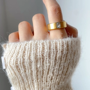 Close-up of matte gold titanium ring with square zircon on a soft knit sweater background
