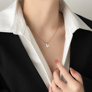 Close-up of a white heart enamel necklace on model wearing a white shirt and black blazer