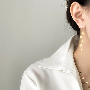 Detail of golden willow leaf tassel earrings and necklace set on a model in white shirt
