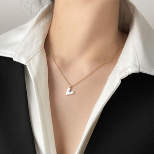 Close-up of minimalist gold thin chain necklace with white enamel heart pendant on a woman