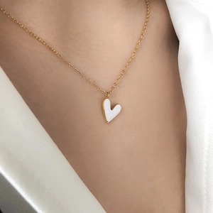 Close-up of white enamel heart pendant on a gold chain necklace worn by a model