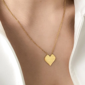 Detail shot of golden pixel heart pendant with grid texture on a model neckline