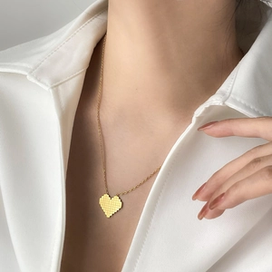 Close-up of golden pixelated heart necklace worn by a model in a minimalist style