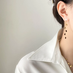 Detail of long gold leaf tassel earrings and necklace set worn by a model in soft light