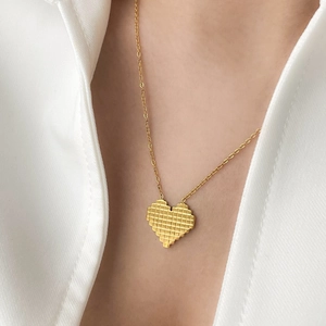 Detailed view of a gold pixel-style heart pendant on a delicate chain worn on a white shirt