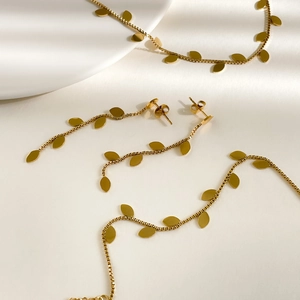 Elegant gold leaf jewelry set including tassel earrings and matching necklace on white satin