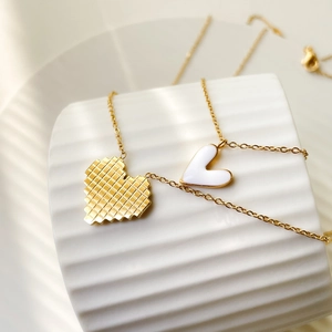 Detailed macro of golden grid heart pendant with white enamel on a white textured surface