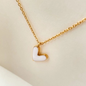 Macro shot of minimalist gold chain necklace with asymmetric white enamel heart pendant