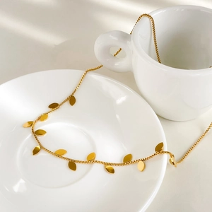 Close-up of golden leaf pendants on a refined box chain necklace over ceramic