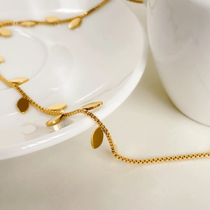 Macro view of gold box chain necklace with oval leaf pendants on white porcelain