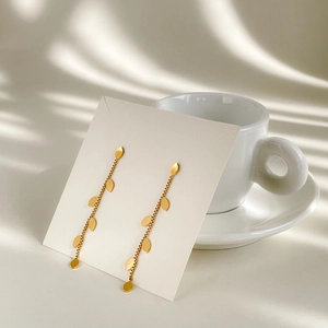 Detail of long gold leaf tassel earrings displayed on white card near coffee cup