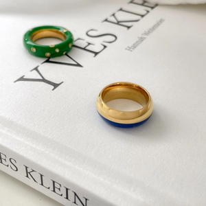 Détail de bague en émail vert avec diamants et bague bicolore bleu-or sur un livre blanc