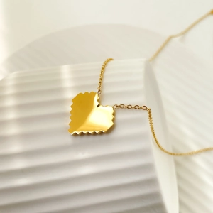Close-up of golden heart pendant necklace with serrated edges on white ceramic background