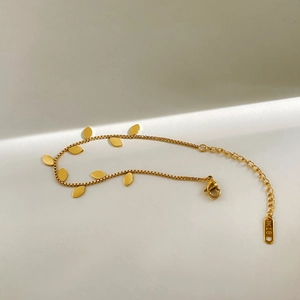 Macro detail of golden leaf bracelet with K18 engraved tag on a minimalist background