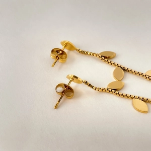 Detailed view of long gold leaf earrings with square chains and reflective oval pendants