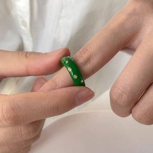 Gros plan d'une bague en émail vert avec diamants dorés portée sur la main