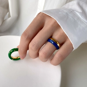 Détail de bagues en émail bleu et vert avec diamants sur une main dans un cadre pur