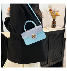 Detail of blue striped crossbody bag with gold flower lock and braided top handle