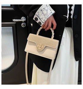 Detail of crossbody bag with gold textured flap and metal flower-shaped twist lock