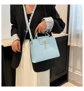 Detail of light blue crossbody bag with crocodile texture and golden deer pendant