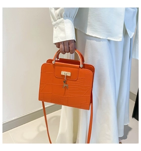 Close-up of orange crocodile pattern crossbody bag with golden deer charm detail