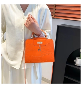 Detail of orange crocodile texture bag featuring a golden deer charm and metal handle