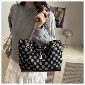 Detail of checkered tweed tote bag with gold chain strap and deer pendant on model