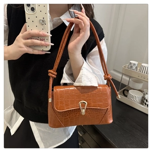 Détail de la texture crocodile et du fermoir doré sur le sac bandoulière marron