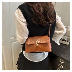 Sac à motif crocodile marron avec boucle dorée porté à l'épaule par un mannequin