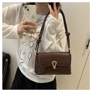 Detail of a brown crocodile pattern shoulder bag with a gold horseshoe lock and knotted strap
