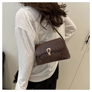 Detail of brown crocodile pattern shoulder bag with gold buckle and textured leather finish