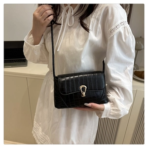 Detail of black crocodile texture handbag with gold horseshoe buckle on model