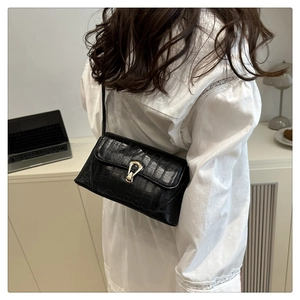 Détail du sac noir à motif crocodile avec boucle fer à cheval dorée porté à l'épaule