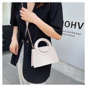 Detail of white crocodile pattern handbag with circular handle and gold chain strap