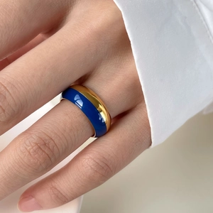 Détail d'une bague large en émail bleu et plaqué or portée avec une chemise blanche chic