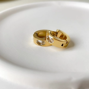 Gros plan de boucles d'oreilles dorées en C avec zircons ovales et texture nacrée
