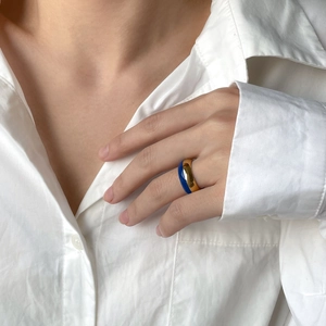 Détail d'une bague dorée en émail bleu au doigt montrant un design vintage épuré