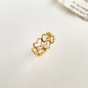 Détail de la bague en or avec motif de cœurs évidés sur un fond texturé blanc épuré