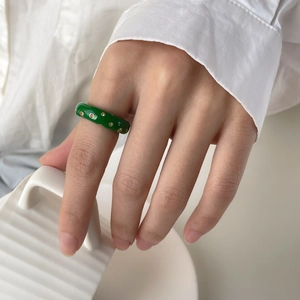 Gros plan d'une bague en émail vert avec points dorés et diamants sur le doigt