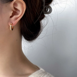 Gros plan de boucles d'oreilles créoles dorées en C avec zircons baguettes sur oreille