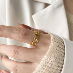 Gros plan d'une bague ajourée en forme de cœur dorée mate portée au doigt