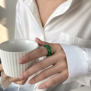 Gros plan d'une bague en émail vert avec clous dorés portée sur un doigt