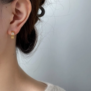 Gros plan d'une boucle d'oreille huggie dorée sertie de zircon porté sur un lobe