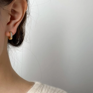 Détail d'une boucle d'oreille dorée en C avec incrustation blanche portée par un mannequin