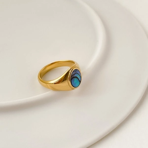 Vue détaillée d'une bague dorée vintage avec pierre ovale en nacre bleue sur plateau blanc