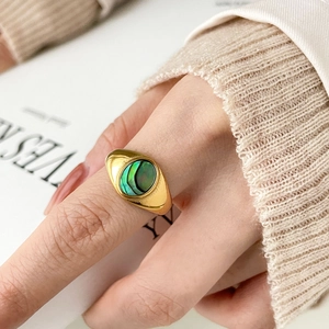 Gros plan d'une bague dorée en zircon avec incrustation de nacre ovale au doigt