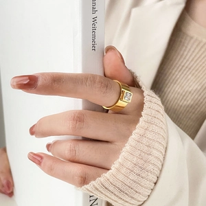Détail d'une bague large dorée avec zircone carrée portée par un mannequin lisant